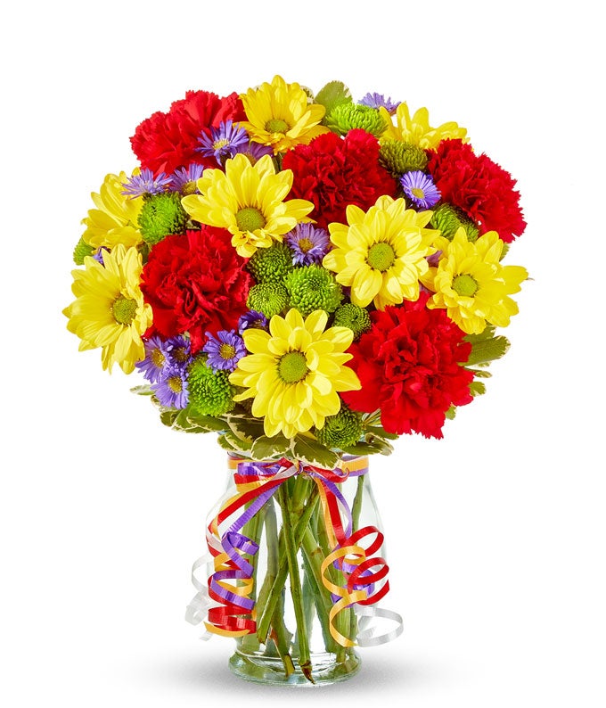 Yellow daisies, red carnations and green button poms in a glass vase